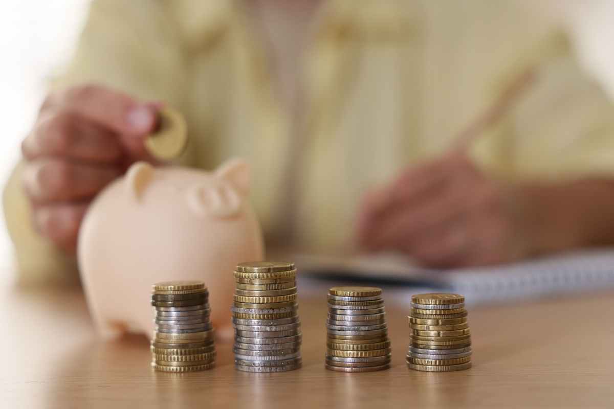 mano di anziano mette spicci in un salvadanaio