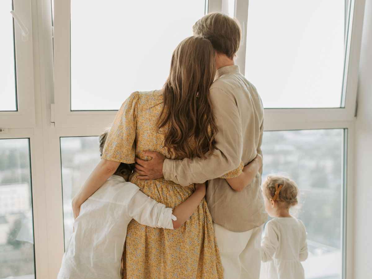 una famiglia si abbraccia e guarda fuori dalla finestra